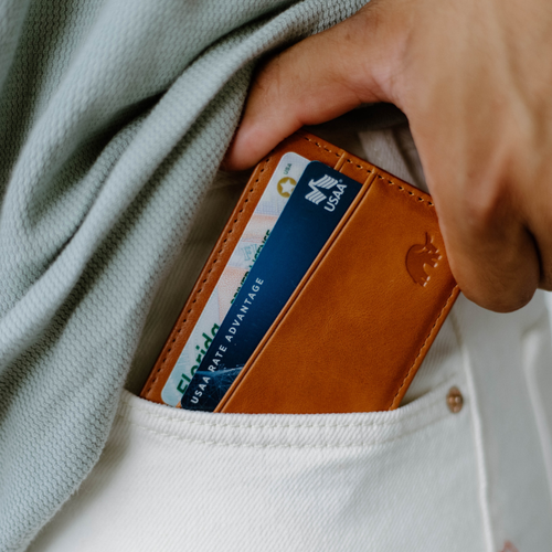 A person placing a leather magnetic wallet in a pocket, showing cards partially visible.